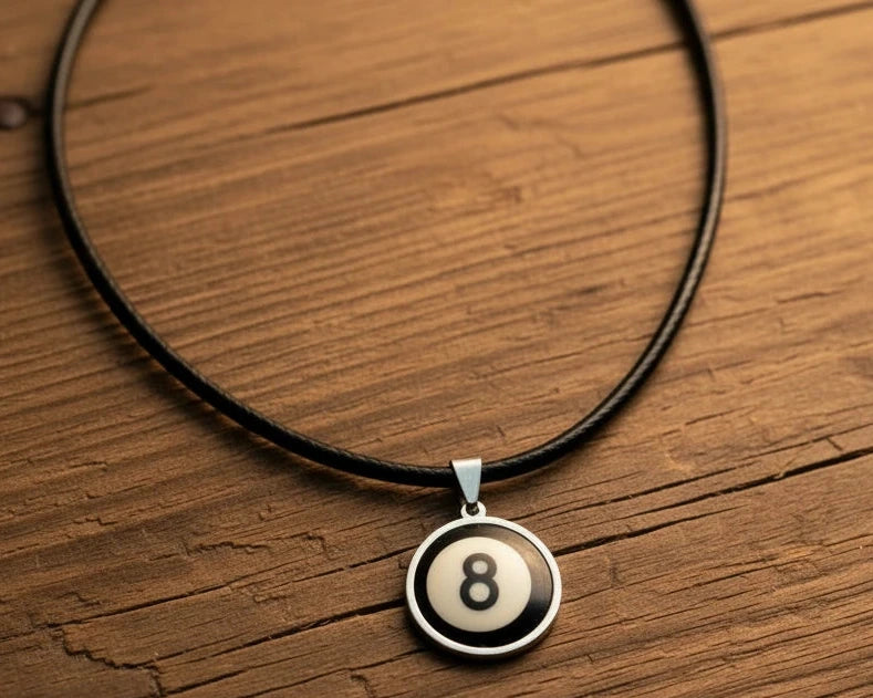 A black cord necklace with a circular pendant featuring an 8-ball design, displayed on a rustic wooden surface.
