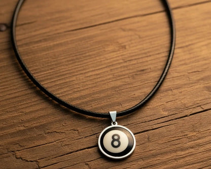 A black cord necklace with a circular pendant featuring an 8-ball design, displayed on a rustic wooden surface.