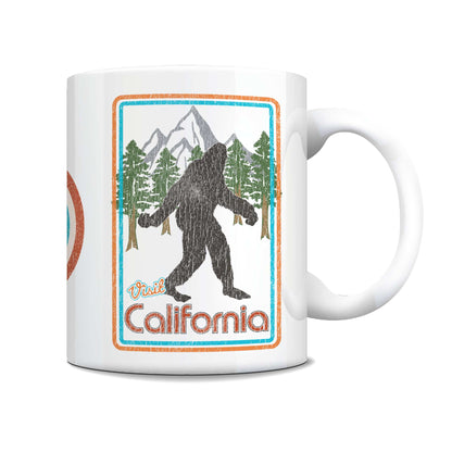A white ceramic coffee mug featuring a retro-style California Bigfoot graphic with mountains, pine trees, and the text 'Paul California' in orange and blue.