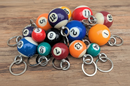 A pile of miniature billiard balls keychains with silver metal key rings, displayed on a light-colored wooden surface.