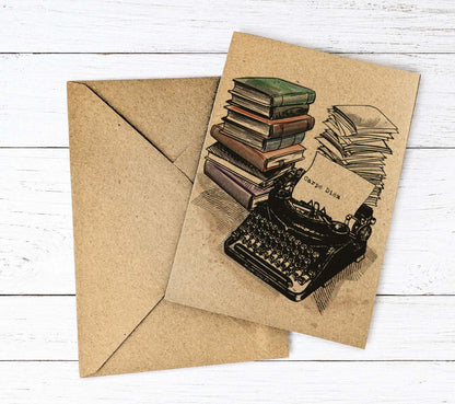 A kraft paper greeting card with an illustration of a typewriter, books, and stacks of papers, shown with a matching kraft envelope on a white wood background.