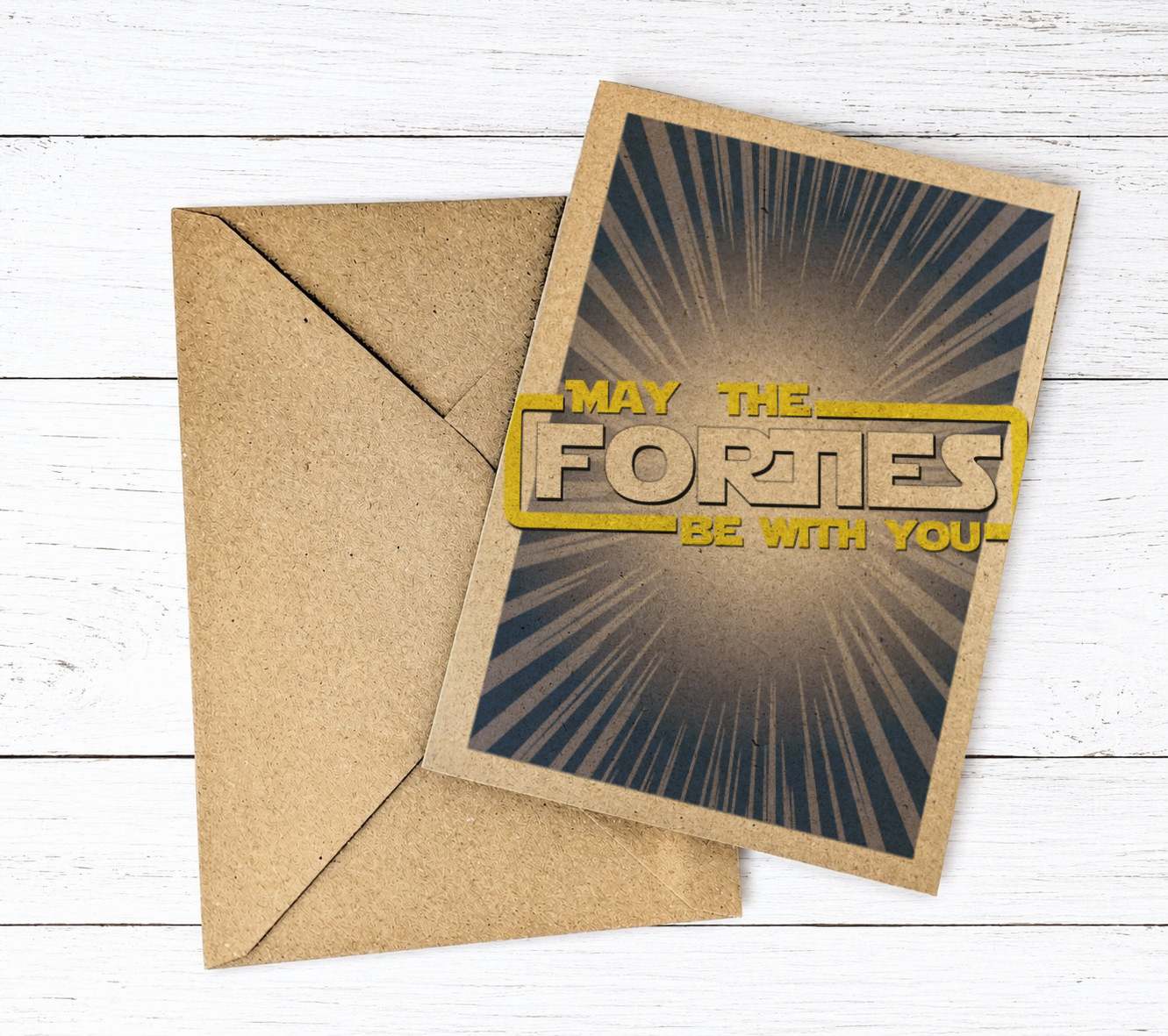 A square kraft paper greeting card with a brown envelope, placed on a white wood plank background. The card features a dark gray and black sunburst design with the text 'MAY THE FORTIES BE WITH YOU' in yellow and beige.