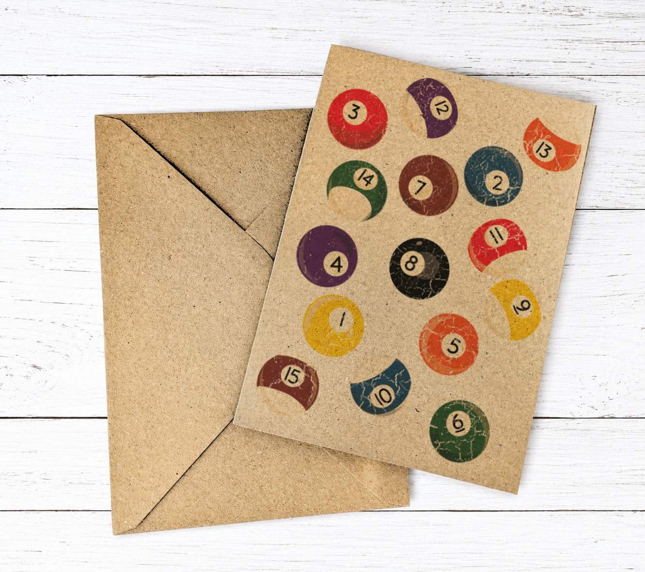 A square kraft paper greeting card with a vintage-style illustration of colorful pool balls, shown with a matching brown envelope on a white wood plank background.