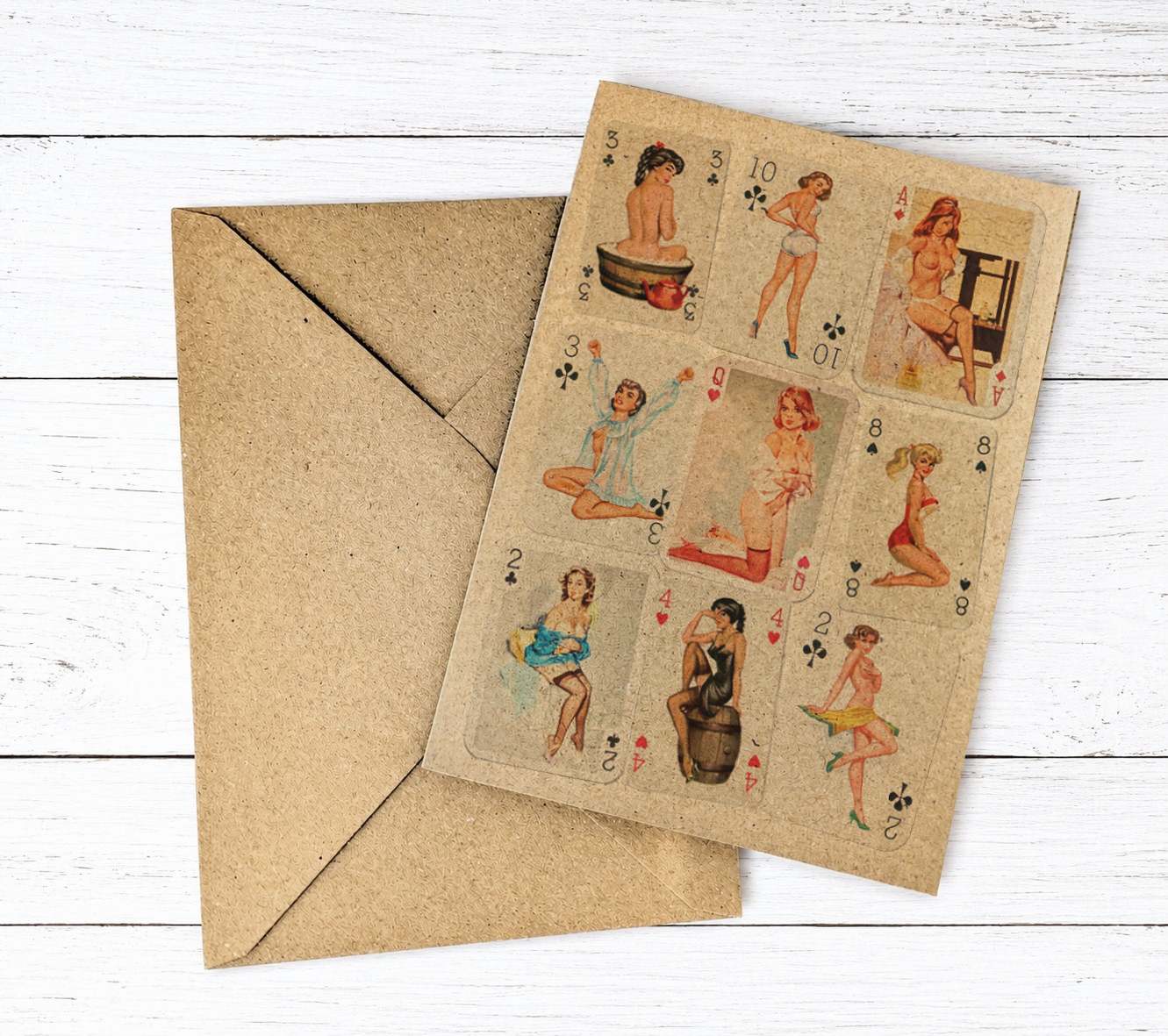 A vintage-style playing card deck or card set with illustrated pin-up women on a tan cardstock, shown with a matching brown kraft envelope on a white wood plank background.