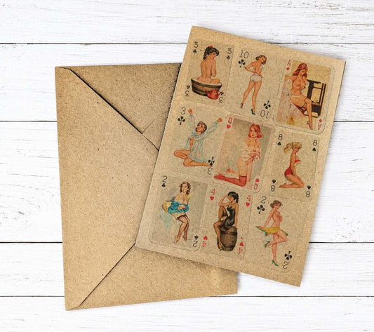 A vintage-style playing card deck or card set with illustrated pin-up women on a tan cardstock, shown with a matching brown kraft envelope on a white wood plank background.
