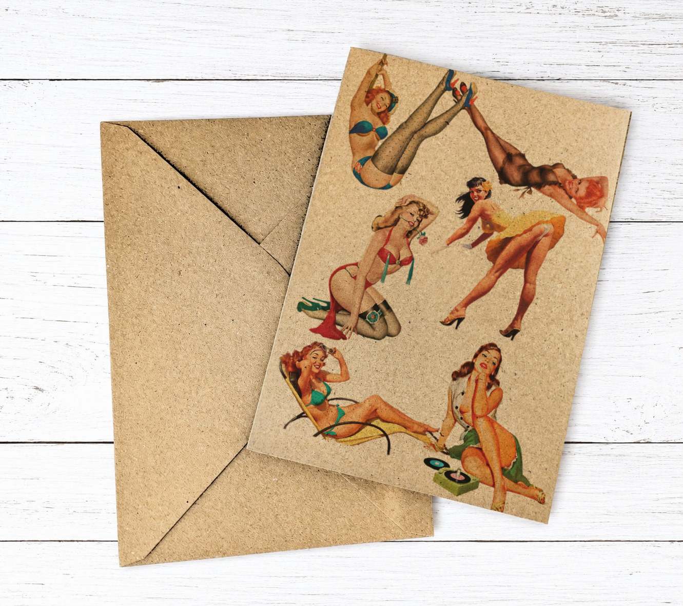 A kraft paper envelope lies behind a matching card printed with retro pin-up women in bikinis, photographed on a white wood plank background.