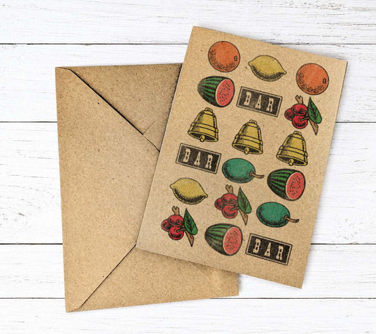 A kraft paper greeting card with vintage-style fruit slot machine logos illustrations of lemons, watermelons, bells, cherries, and the word 'BAR' repeated, shown with a matching kraft envelope on a white wood background.