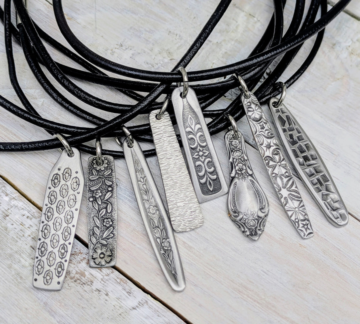 Necklace with multiple stainless steel cutlery pendants with leather necklace on a wooden surface