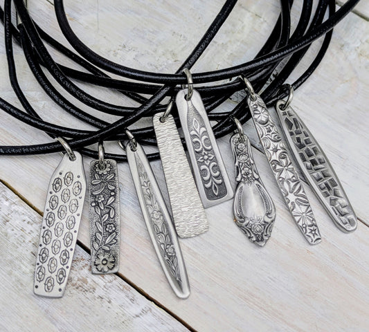 Necklace with multiple stainless steel cutlery pendants with leather necklace on a wooden surface