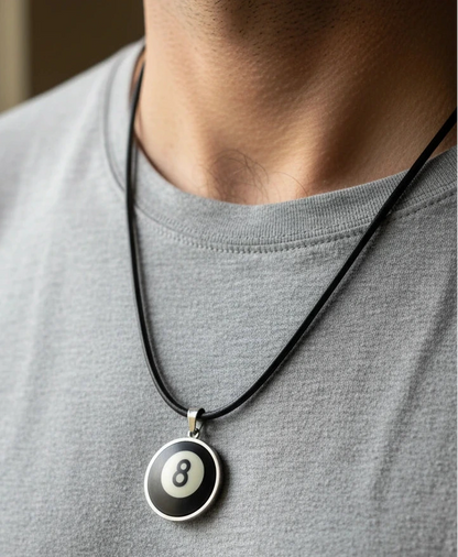 A close-up of a person wearing a black cord necklace with a round pendant featuring a black, white, and silver 8-ball design.